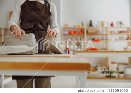 Close up of ceramist woman wearing apron is preparing clay to make pottery pieces in her studio 111091060