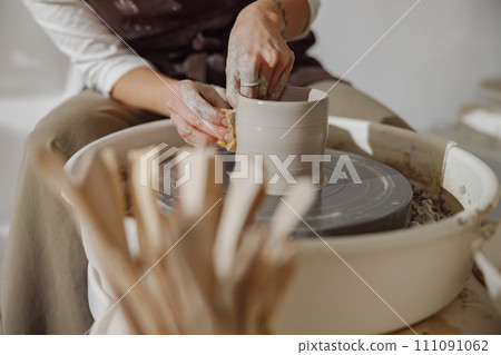 Close up of hands of professional potter molding pot shape on pottery wheel. Ceramics art concept Close up of hands of professional potter molding pot shape on pottery wheel. Ceramics art concept 111091062