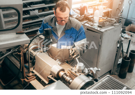 Portrait of professional turner at work on lathe in workshop. 50-55 year old turner in overalls and Portrait of professional turner at work on lathe in workshop. 50-55 year old turner in overalls and 111092094