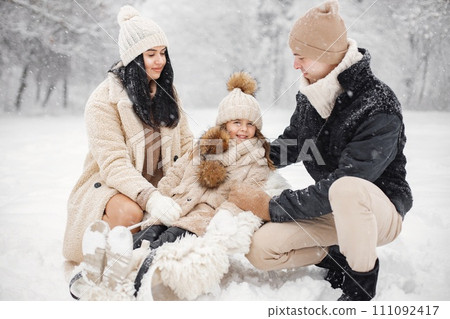 Little girl, father and mother playing outdoors at winter day. Brunette young woman, man and little girl in winter in warm jackets walk in the park with a sled. Mother and daughter wearing winter Little girl, father and mother playing outdoors at winter day. Brunette young woman, man and little girl in winter in warm jackets walk in the park with a sled. Mother and daughter wearing winter 111092417