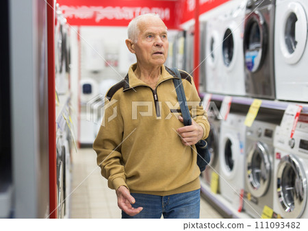 Senior man pensioner buying washing machine in showroom of electrical appliance store 111093482
