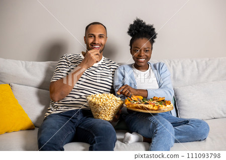 Man and woman family enjoying movie on weekend eating pizza and popcorn while sitting on couch Man and woman family enjoying movie on weekend eating pizza and popcorn while sitting on couch 111093798