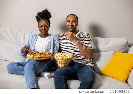 Couple eating pizza and popcorn watching comedy film sitting on couch indoor 111093802
