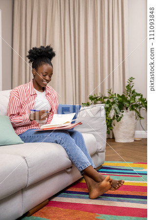 Woman writing to do list or plan for day while sitting on couch in home interior. Woman writing to do list or plan for day while sitting on couch in home interior. 111093848