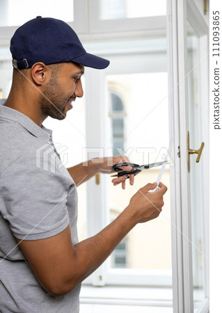 Man putting sealing foam tape on window indoors insulating his house. 111093865