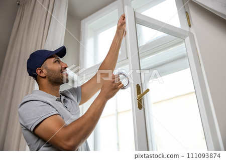 Man putting sealing foam tape on window indoors insulating his house. Man putting sealing foam tape on window indoors insulating his house. 111093874