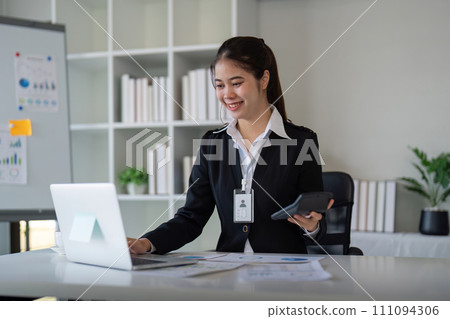 Charming Asian business woman sitting working on laptop in office Charming Asian business woman sitting working on laptop in office 111094306