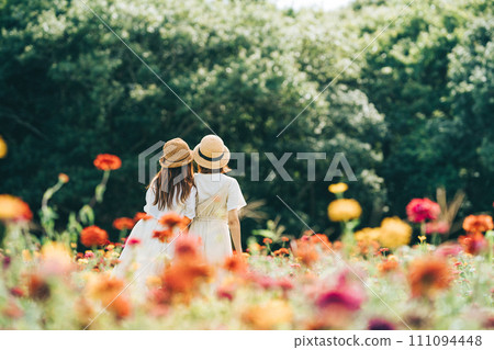 Two girls in straw hats and white dresses in a flower field 111094448