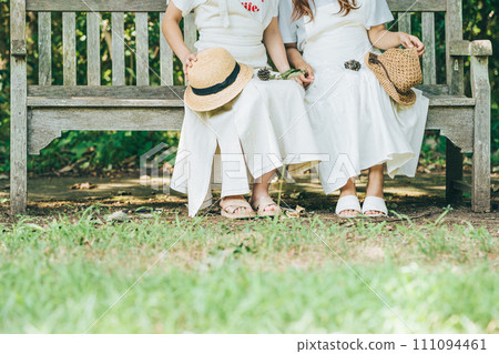 兩個穿著白色洋裝、戴著草帽的女人坐在長椅上 兩個穿著白色洋裝、戴著草帽的女人坐在長椅上 111094461