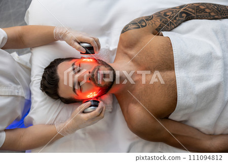 Dark-haired bearded man receiving phototherapy in a clinic 111094812