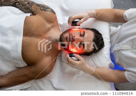 Dark-haired bearded man receiving phototherapy in a clinic 111094814
