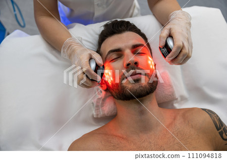 Dark-haired bearded man receiving phototherapy in a clinic Dark-haired bearded man receiving phototherapy in a clinic 111094818