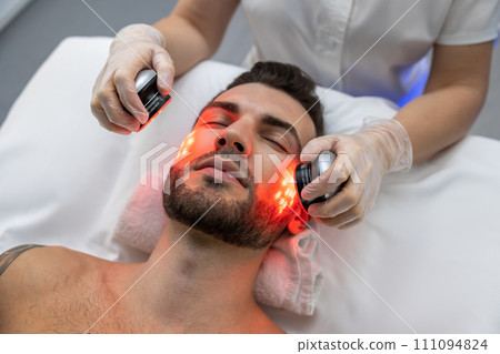 Dark-haired bearded man receiving phototherapy in a clinic 111094824