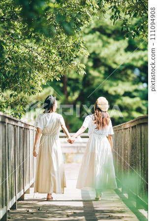 Vertical photo of two girls walking on a bridge holding hands 111094908