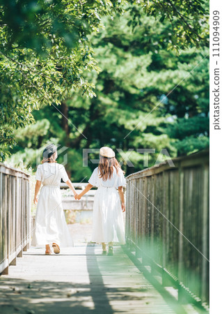 Vertical photo of two girls walking on a bridge holding hands 111094909