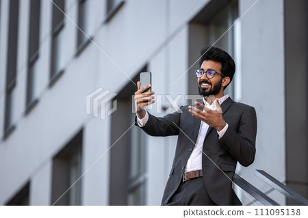 Brunette hindu young man on the building background with phone in hand Brunette hindu young man on the building background with phone in hand 111095138