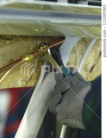 worker hands in gloves joining cooper pipes of an air conditioner using wrenches 111095903