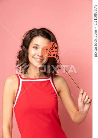 Portrait of young lady stands on pink background with heart shapped decoration Portrait of young lady stands on pink background with heart shapped decoration 111096575