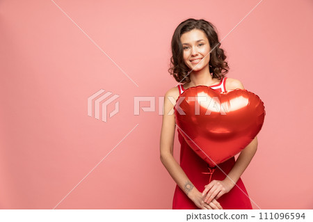 Portrait of young lady stands on pink background with heart shapped red balloon Portrait of young lady stands on pink background with heart shapped red balloon 111096594