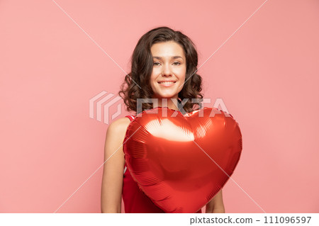 Portrait of young lady stands on pink background with heart shapped decoration Portrait of young lady stands on pink background with heart shapped decoration 111096597