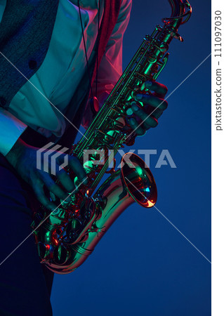Jazz in modern music. Close-up cropped photo of young handsome man playing saxophone in neon light. Gel portraits. 111097030