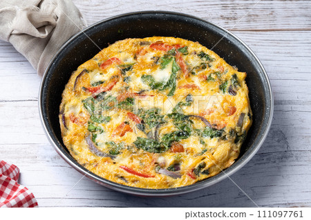 Italian Frittata made with spinach, tomatoes, onion and peppers on white wooden table 111097761