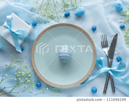 Festive Easter table setting with eggs, flowers and gift box on blue background 111098199