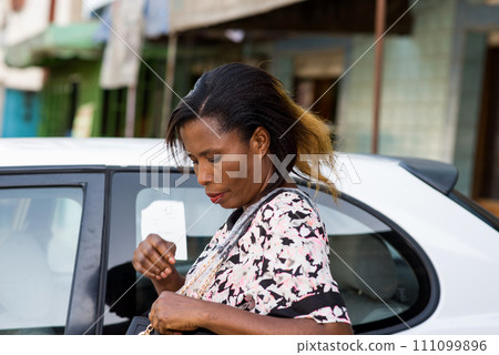 Young happy smiling woman standing in front of a new luxury car and look in his handbag. Young happy smiling woman standing in front of a new luxury car and look in his handbag. 111099896