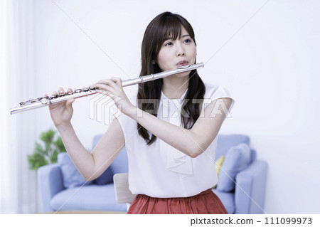 Woman playing the flute in the living room Woman playing the flute in the living room 111099973