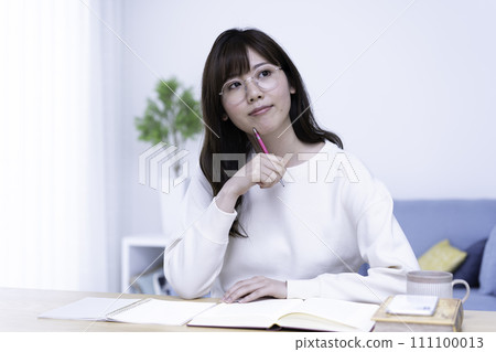 A woman wearing glasses studying in a bright living room A woman wearing glasses studying in a bright living room 111100013