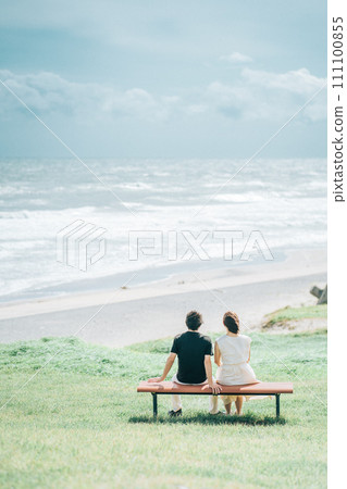 Vertical photo of a couple sitting on a bench and looking at the sea Vertical photo of a couple sitting on a bench and looking at the sea 111100855