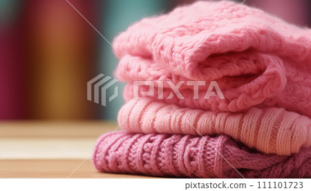 Stack of cozy pink knit sweaters on a wooden surface against a blurred background. 111101723