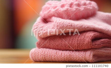 Stack of cozy pink knit sweaters on a wooden surface against a blurred background. 111101740