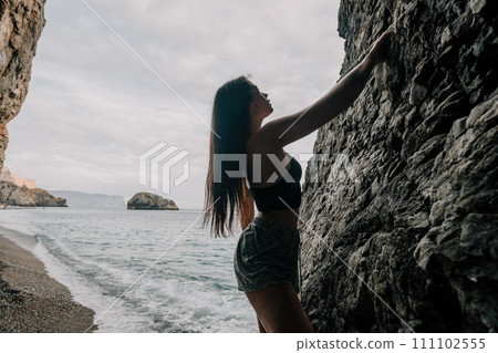 Sports Woman Climbing The Rock. Young woman With slim fit body climbing in volcanic basalt cave with beautiful sea view. The athlete girl trains in nature. Woman overcomes difficult climbing route. Sports Woman Climbing The Rock. Young woman With slim fit body climbing in volcanic basalt cave with beautiful sea view. The athlete girl trains in nature. Woman overcomes difficult climbing route. 111102555