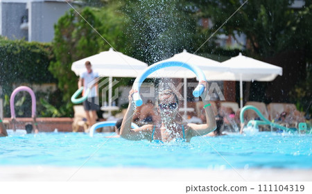 Young woman knocking noodle on water of swimming pool on aqua aerobics Young woman knocking noodle on water of swimming pool on aqua aerobics 111104319