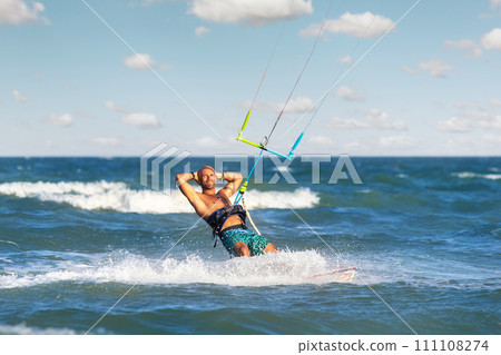 Portrait young adult caucasian fit male person enjoy riding kite surf board making fun trick stunt bright sunny day against blue sky at sea ocean shore. Watersport adrenaline fun adventure acitivity Portrait young adult caucasian fit male person enjoy riding kite surf board making fun trick stunt bright sunny day against blue sky at sea ocean shore. Watersport adrenaline fun adventure acitivity 111108274