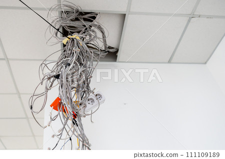 Electrical wires hanging from the ceiling. Cables hanging from ceiling of room. Building under construction. 111109189