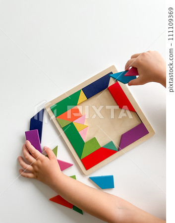 childs hand collects multicolored wooden mosaic on white background. 111109369
