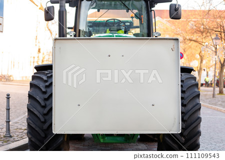 Front view of a tractor with a blank white sign, parked on a city street. Farmers union protest strike against government Policy in Germany Europe. Mockup place for text message 111109543