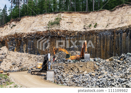 Basalt mining. Yellow excavators in a basalt quarry near the forest. 111109982