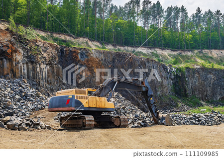 Basalt mining. Yellow excavators in a basalt quarry near the forest. Basalt mining. Yellow excavators in a basalt quarry near the forest. 111109985