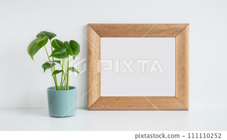 Wooden mock up photo frame and Monstera deliciosa or Swiss Cheese Plant in a blue flower pot on a white table background 111110252