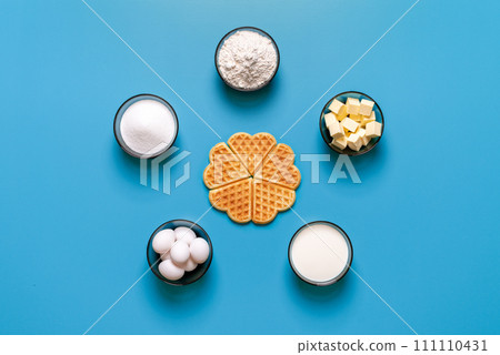 Waffle baking ingredients top view, isolated on a blue background Waffle baking ingredients top view, isolated on a blue background 111110431