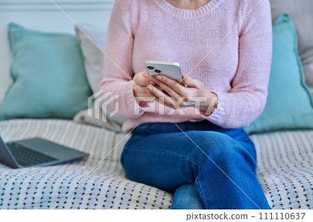 Close-up of smartphone in hands of woman sitting on couch at home Close-up of smartphone in hands of woman sitting on couch at home 111110637