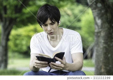 A foreign man reading while listening to music in a fresh green park A foreign man reading while listening to music in a fresh green park 111111199