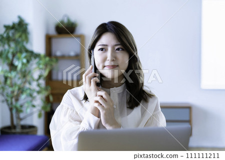 一位年輕女子在客廳使用筆記型電腦時用智慧型手機交談 111111211