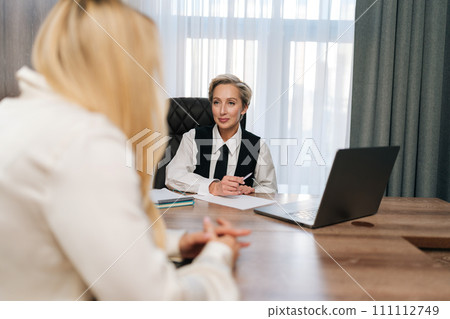 View from shoulder of unrecognizable female job seeker sitting at desk with middle-aged woman hr at office, speak about describe experience. Confident woman candidate on vacant place answer question. View from shoulder of unrecognizable female job seeker sitting at desk with middle-aged woman hr at office, speak about describe experience. Confident woman candidate on vacant place answer question. 111112749