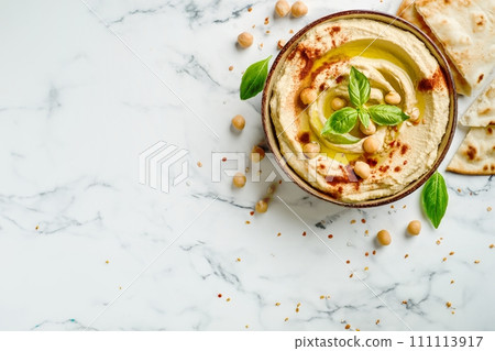 Top view of traditional hummus from chickpea beans with oil in a bowl on white marble background Top view of traditional hummus from chickpea beans with oil in a bowl on white marble background 111113917
