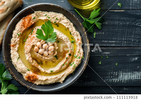 Top view of traditional hummus from chickpea beans with oil in a bowl on black wooden background 111113918