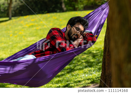 Brunette young man sleeping in hammock in the park Brunette young man sleeping in hammock in the park 111114168